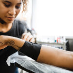 tattoo shop artist wrapping her customer's arm with lightning x black self adherent bandage wrap