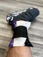 Instant cold pack secured to a man's ankle with black self-adherent wrap