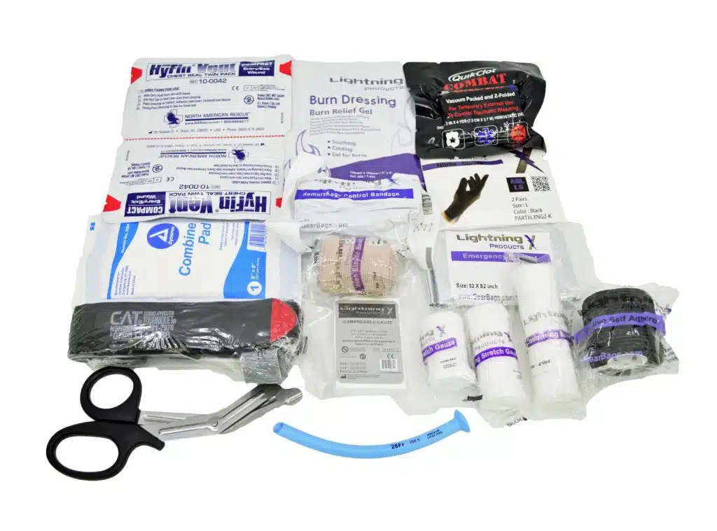 Assortment of trauma supplies including a tourniquet, shears, dressings, airway and rolled bandages.